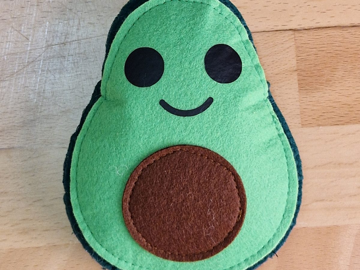 Die fertige, gefüllte Filzavocado mit Gesicht und braunem Kern auf einer Holzplatte