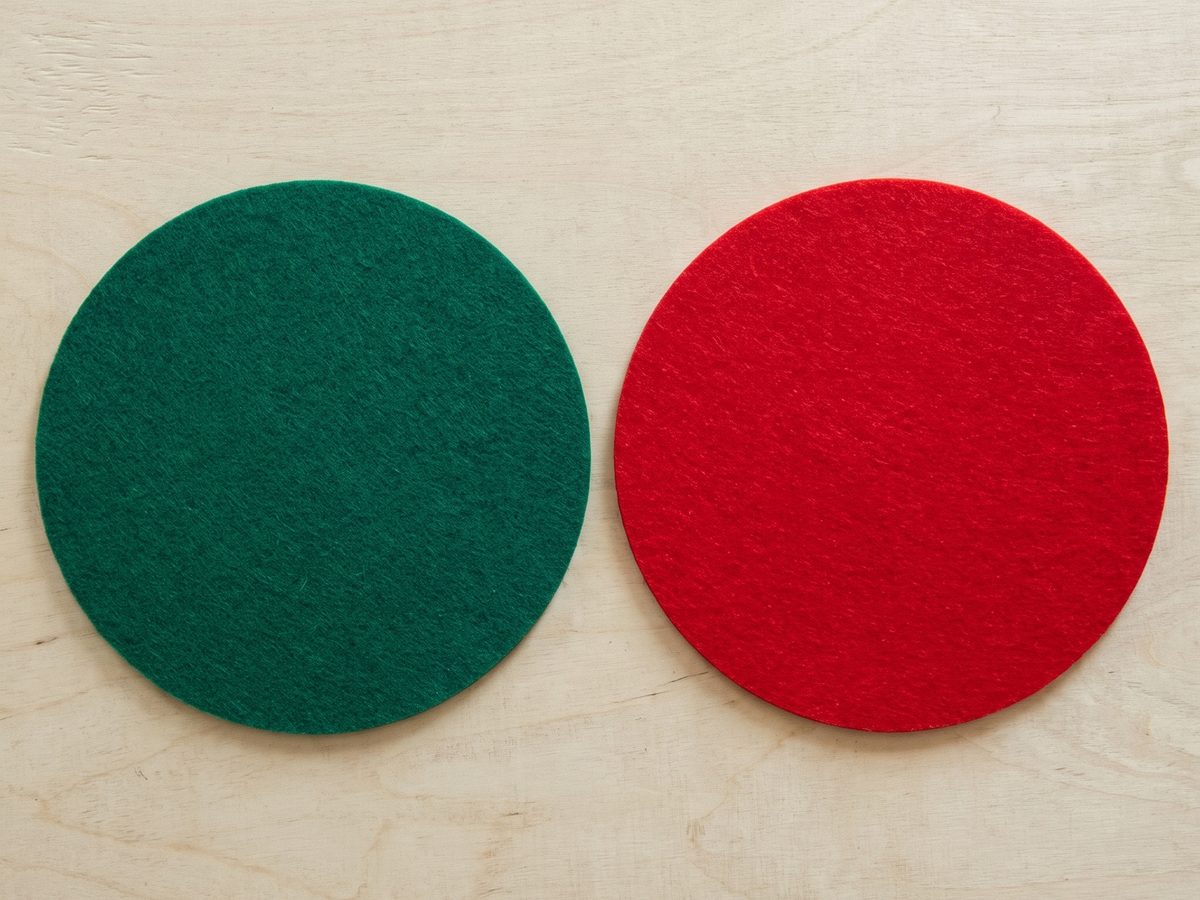 Zwei ausgeschnittene Filzkreise, einer dunkelgrün und einer rot, nebeneinander auf einer hellen Holzplatte